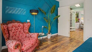 Ein Zimmer mit blauer Akzentwand, einem rot gemusterten Sofa, einer Stehlampe und einem Blumentopf.