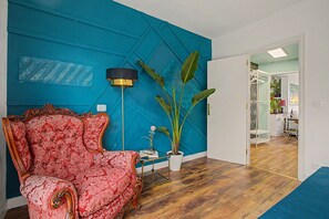 Una habitación con una pared azul de acento, un sofá rojo estampado, una lámpara de pie y una planta en maceta.