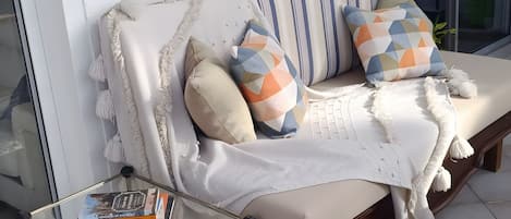 A sofa with cushions, a small table with books, and a wall-mounted light fixture.