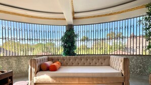 Un balcón soleado con un sofá capitonado, una mesa redonda y vistas al exterior.