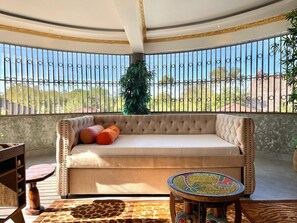 A sunlit balcony with a tufted sofa, a round table, and a view of the outdoors. - Spacious 6-bedroom villa in Diani with a swimming pool and access to the beach (Kwale County)