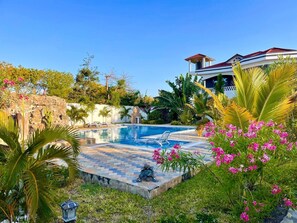 A swimming pool surrounded by lush greenery and a stone wall. - Spacious 6-bedroom villa in Diani with a swimming pool and access to the beach (Kwale County)