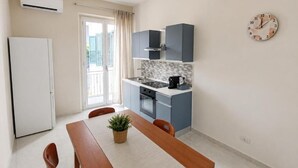 A compact kitchen with a built-in oven, a dining table with chairs, and a clock on the wall. - ETNERA (Trecastagni)