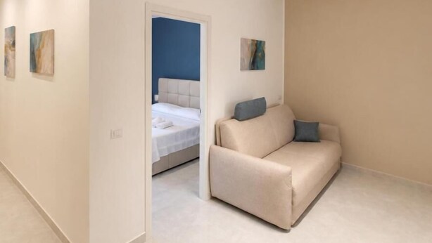 A modern hotel room with a beige sofa, a bed with a blue headboard, and a small painting on the wall. - ETNERA (Trecastagni)