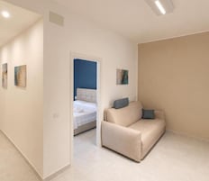 Una camera d'albergo moderna con un divano beige, un letto con testiera blu e un piccolo quadro appeso al muro.