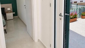 A corridor leading to a balcony with a view of a building and potted plants. - ETNERA (Trecastagni)