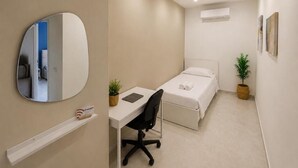 A compact bedroom with a single bed, a desk, a chair, a bedside plant, and a wall-mounted mirror. - ETNERA (Trecastagni)