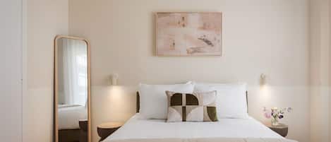 A bedroom with a bed, a bedside table, a nightstand, a wall-mounted artwork, and a mirror.
