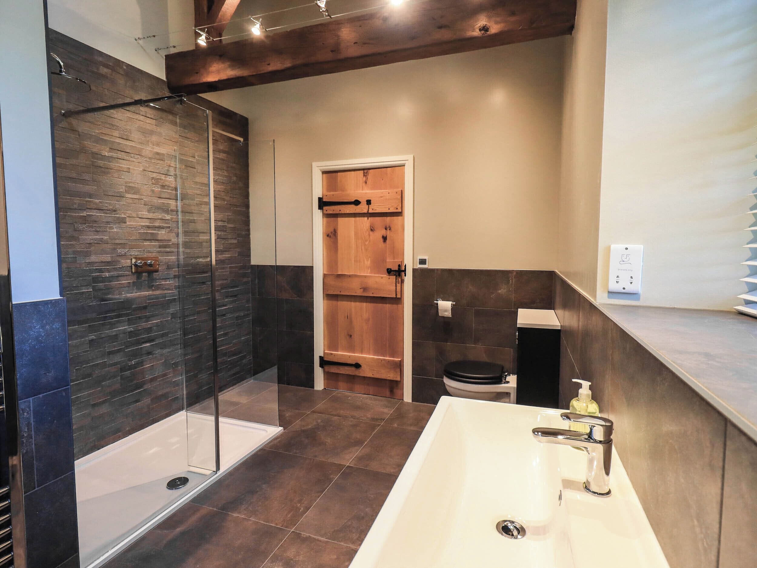 A modern bathroom with a glass shower enclosure, a wooden door, a white sink with a soap dispenser, and a towel rack.