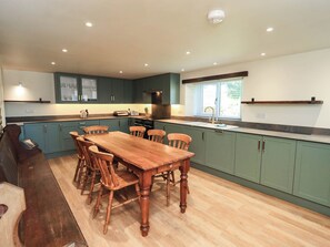 A kitchen with a wooden dining table, green cabinets, and a window with blinds.