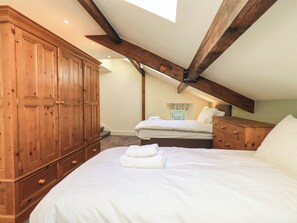 A bedroom with a large wooden wardrobe, a bed with white linens, a smaller bed, and a wooden dresser.