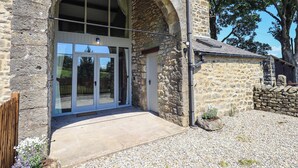 Un edificio de piedra con un amplio arco de entrada, una puerta y un pequeño jardín con guijarros y plantas.