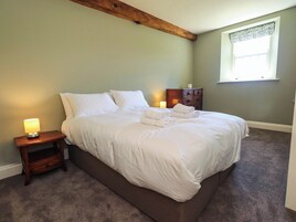 A neatly made bed with white linens and towels, a bedside lamp, a wooden nightstand, and a window with a patterned valance.