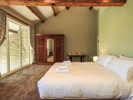 Un dormitorio con una cama grande, un armario de madera, una mesita pequeña y una ventana con cortinas.