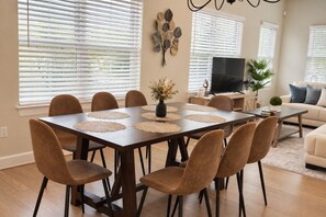A dining area with a rectangular table, multiple chairs, and a television in the background.