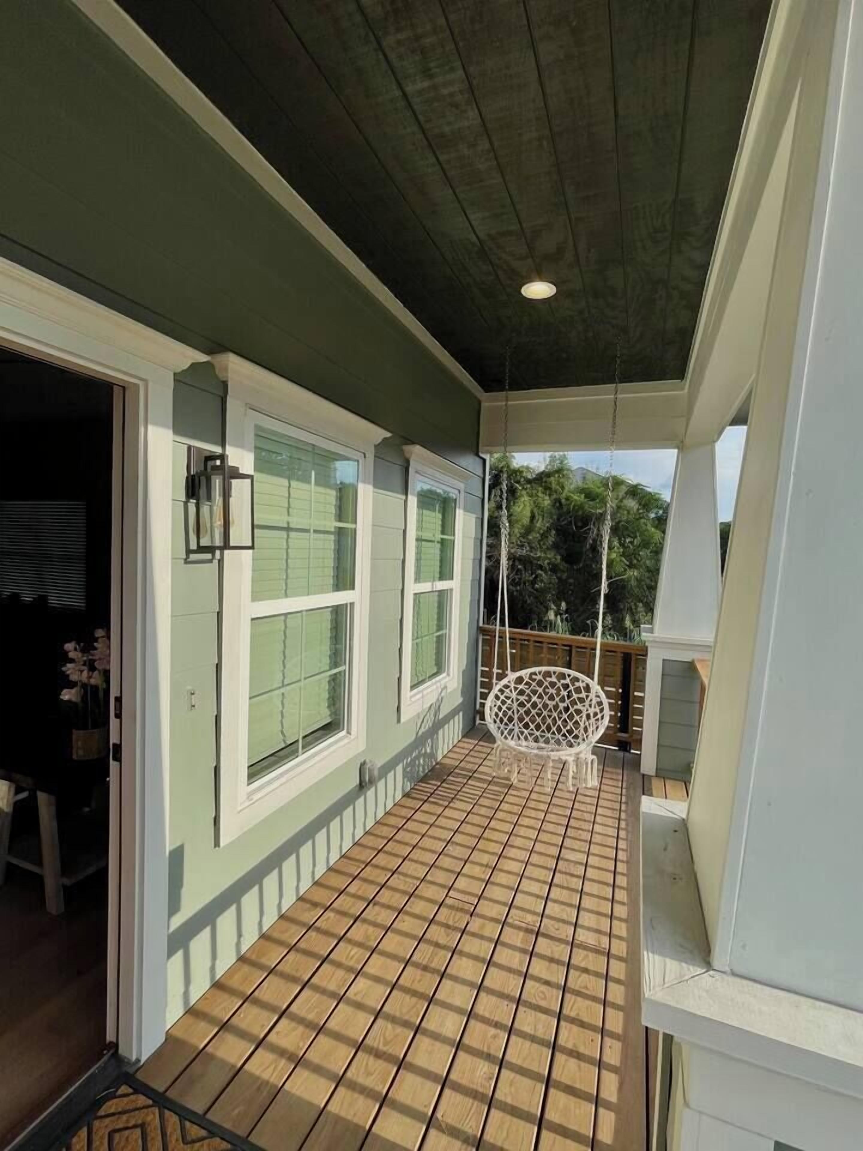 A covered balcony with a swing chair, a wooden floor, and a view of the outdoors.