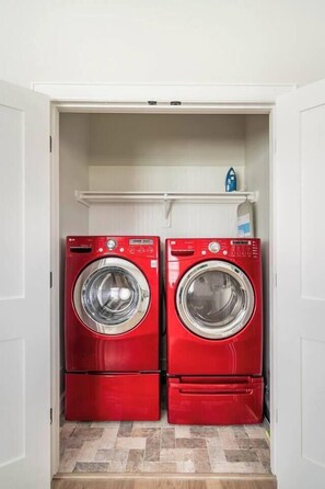 A laundry room with two red washing machines and a white shelf above.