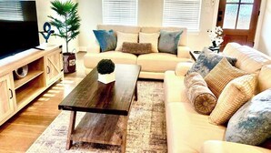 A living room with a sofa, coffee table, TV, and blinds. - Designer Home Near Downtown w/Patio+Board games (Houston)