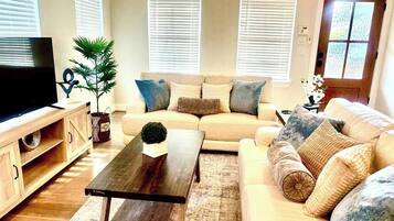 Ein Wohnzimmer mit einer Couch, Couchtisch, Fernseher und Jalousien.