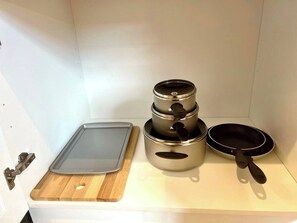 A kitchen with a wooden cutting board, a stack of stainless steel pots, and a frying pan.