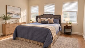 A bedroom with a large bed, a dresser, a nightstand, a lamp, and a painting on the wall.