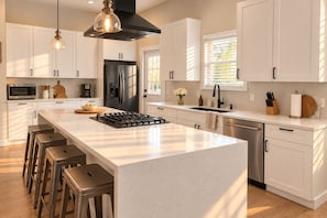 A modern kitchen with white cabinetry, a central island with stools, stainless steel appliances, and pendant lighting.
