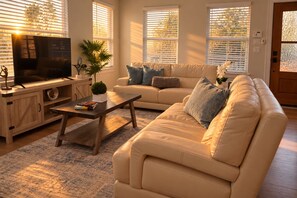 A living room with a sofa, coffee table, TV, and a plant.