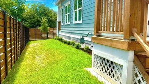 A residential backyard with a wooden deck, a white fence, and a house with blue siding. - Designer Home Near Downtown w/Patio+Board games (Houston)