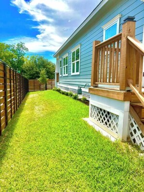 A residential backyard with a wooden deck, a white fence, and a house with blue siding. - Designer Home Near Downtown w/Patio+Board games (Houston)