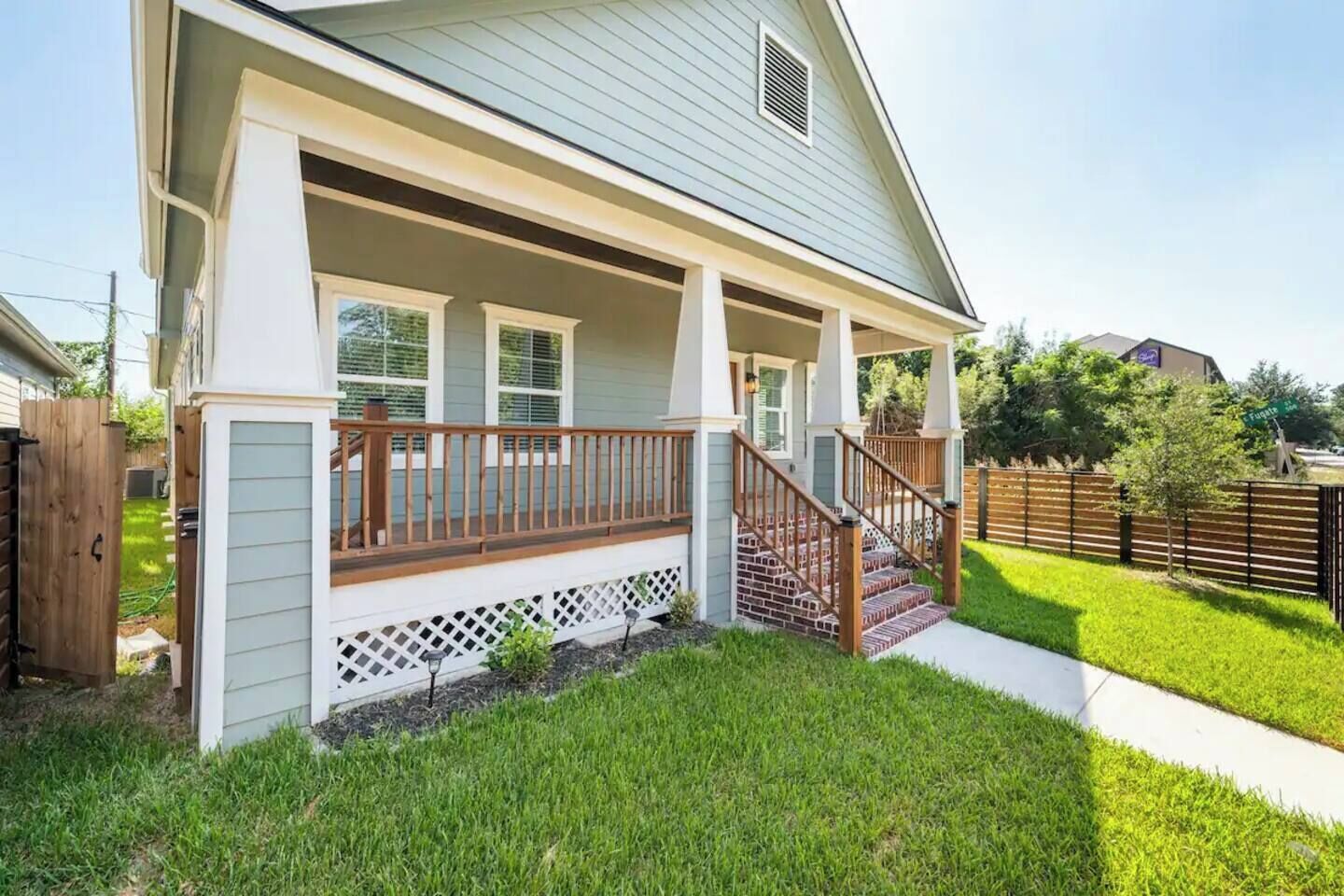 A residential house with a covered porch, a wooden staircase, and a well-maintained lawn.