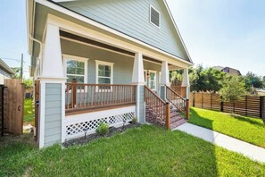 A residential house with a covered porch, a wooden staircase, and a well-maintained lawn. - Designer Home Near Downtown w/Patio+Board games (Houston)