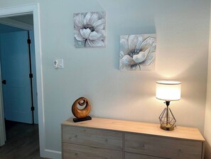 A room with a wooden dresser, a lamp, and two wall-mounted flower paintings.