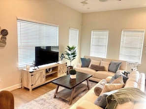 A living room with a TV, sofa, coffee table, and windows.
