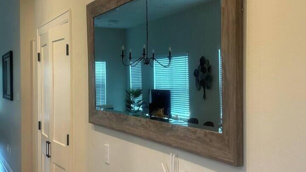 A hallway with a large mirror on the wall, a door on the left, and a small white object on the floor. - Designer Home Near Downtown w/Patio+Board games (Houston)