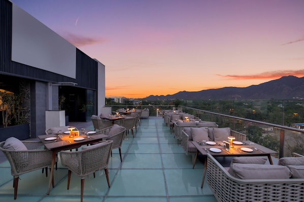 Un área de comedor al aire libre con mesas y sillas, con vistas a un paisaje montañoso.