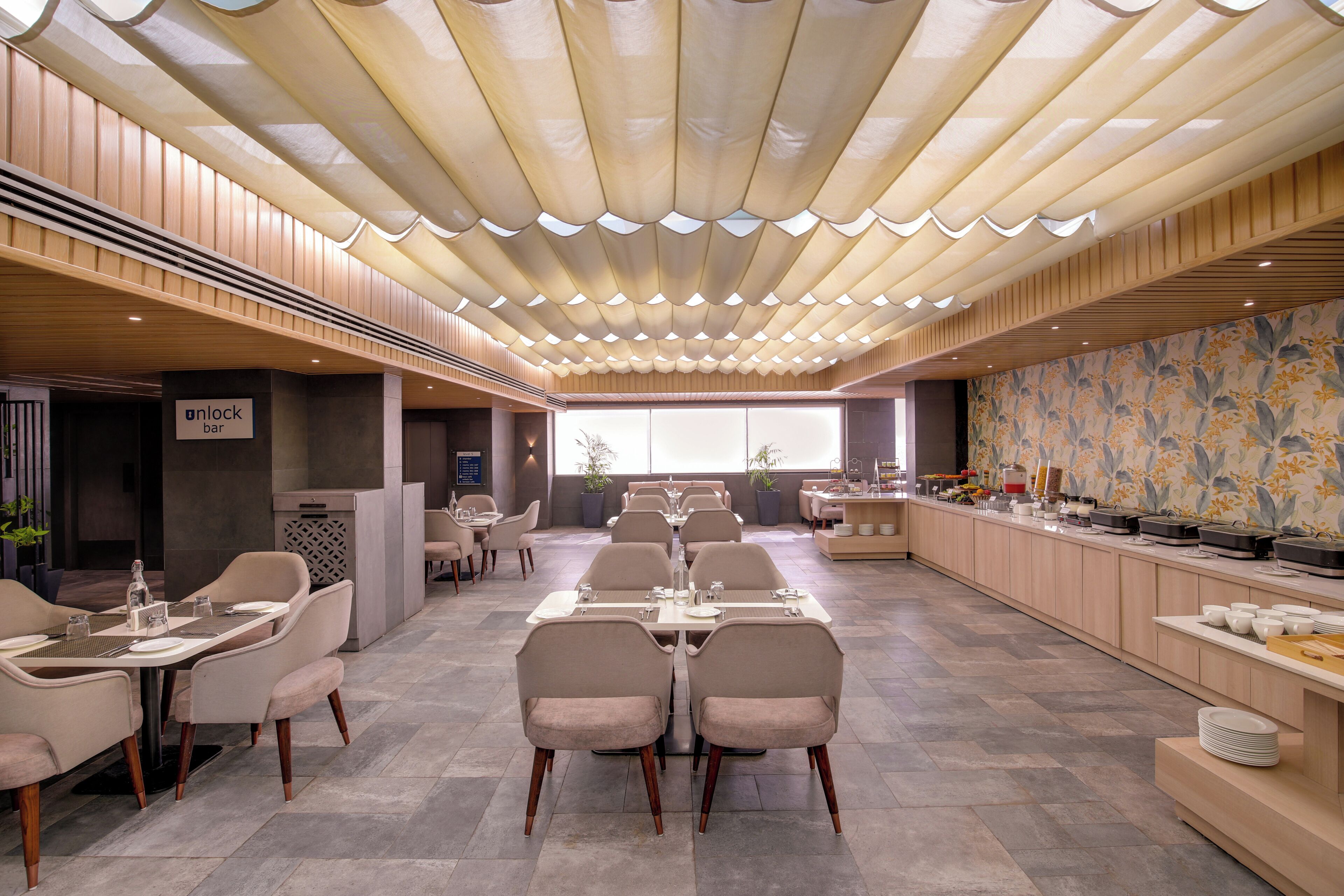 Un restaurante con una barra larga, varias mesas y un techo decorativo.