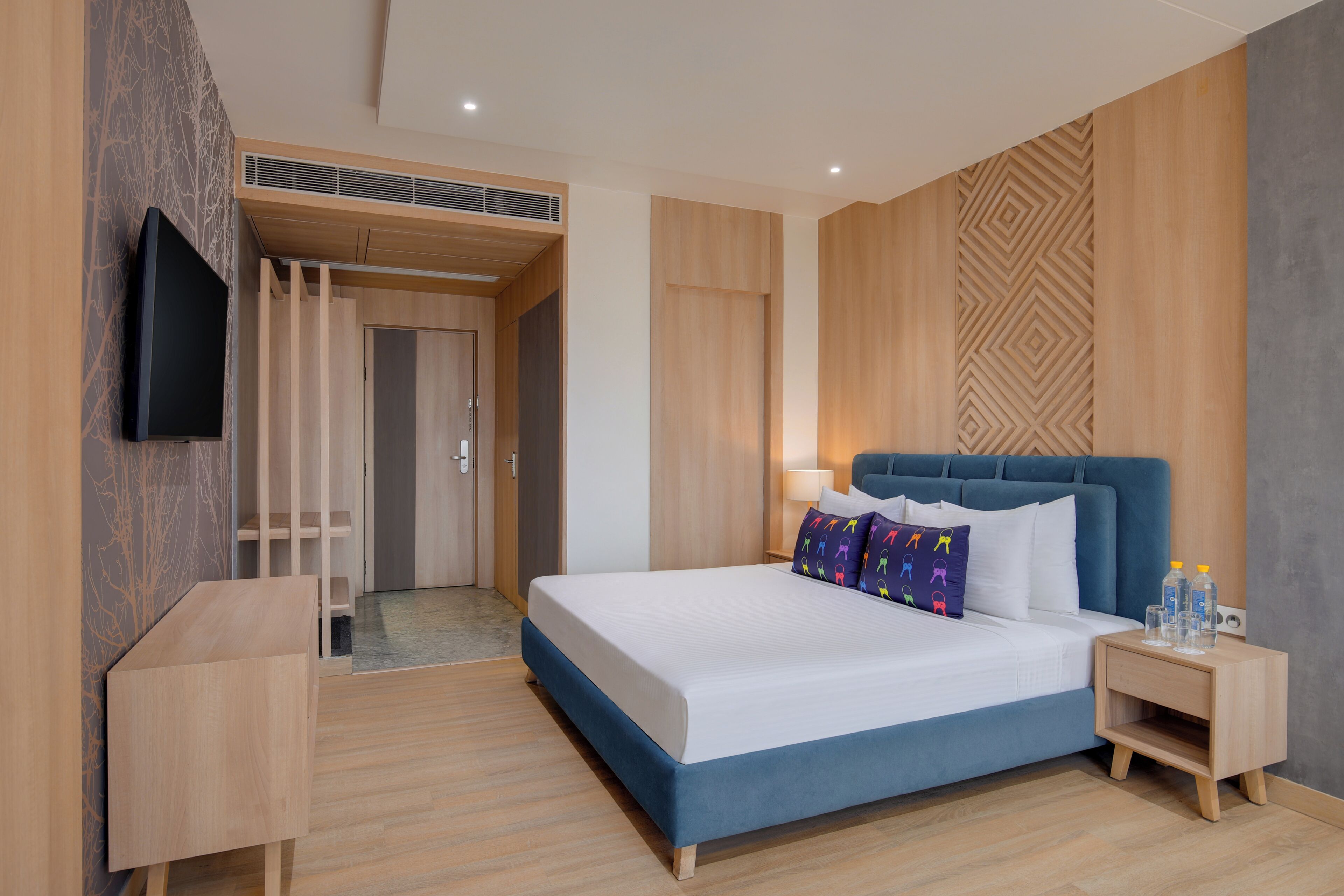 Una habitación de hotel moderna con una cama grande, un televisor montado en la pared y un armario de madera.