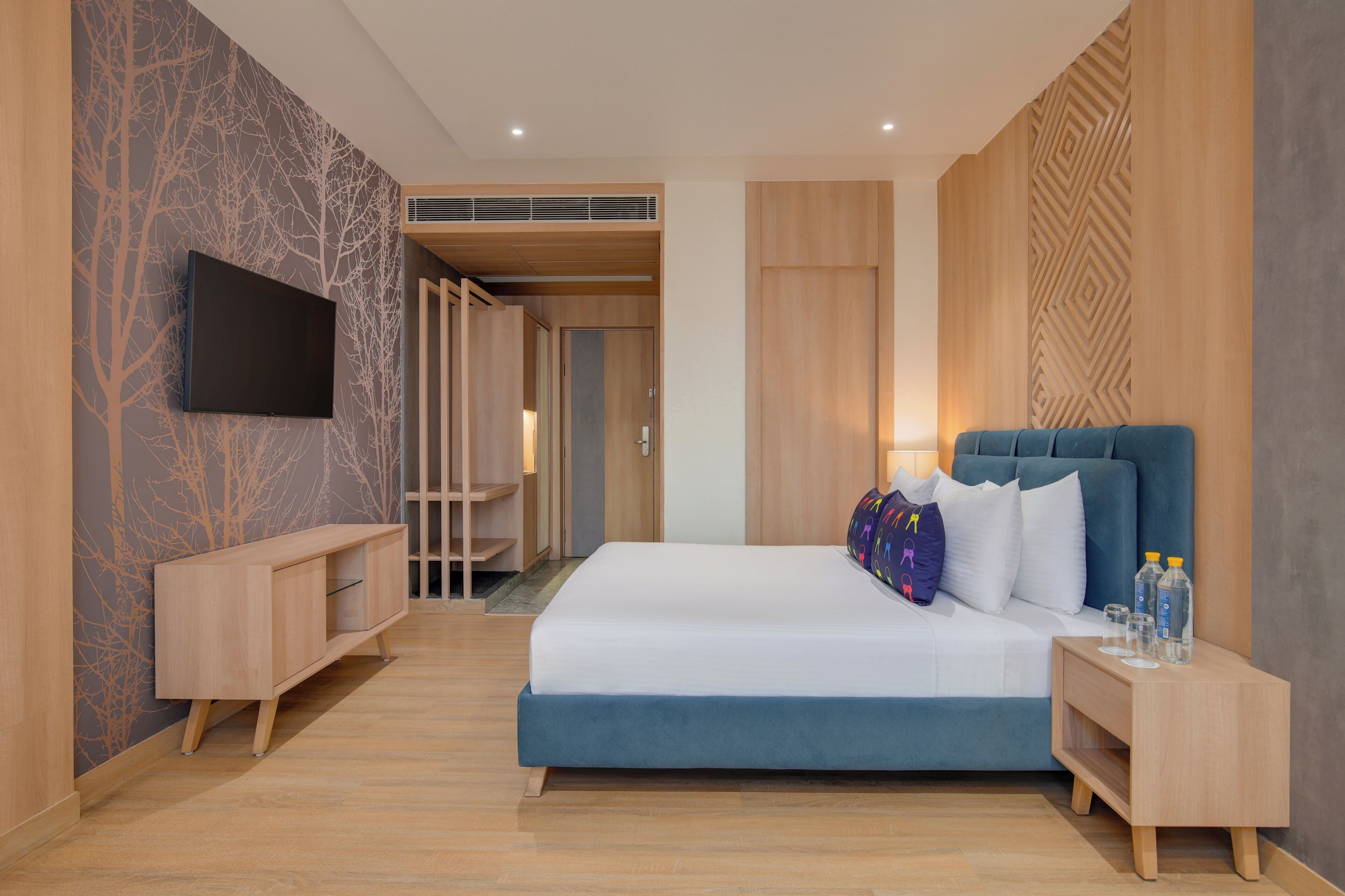 A modern hotel room with a large bed, a TV mounted on the wall, and a wooden wardrobe.