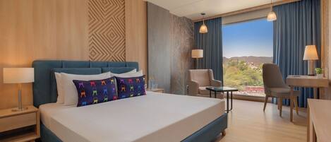 A hotel room with a large bed, a desk, a chair, and a view of the city.