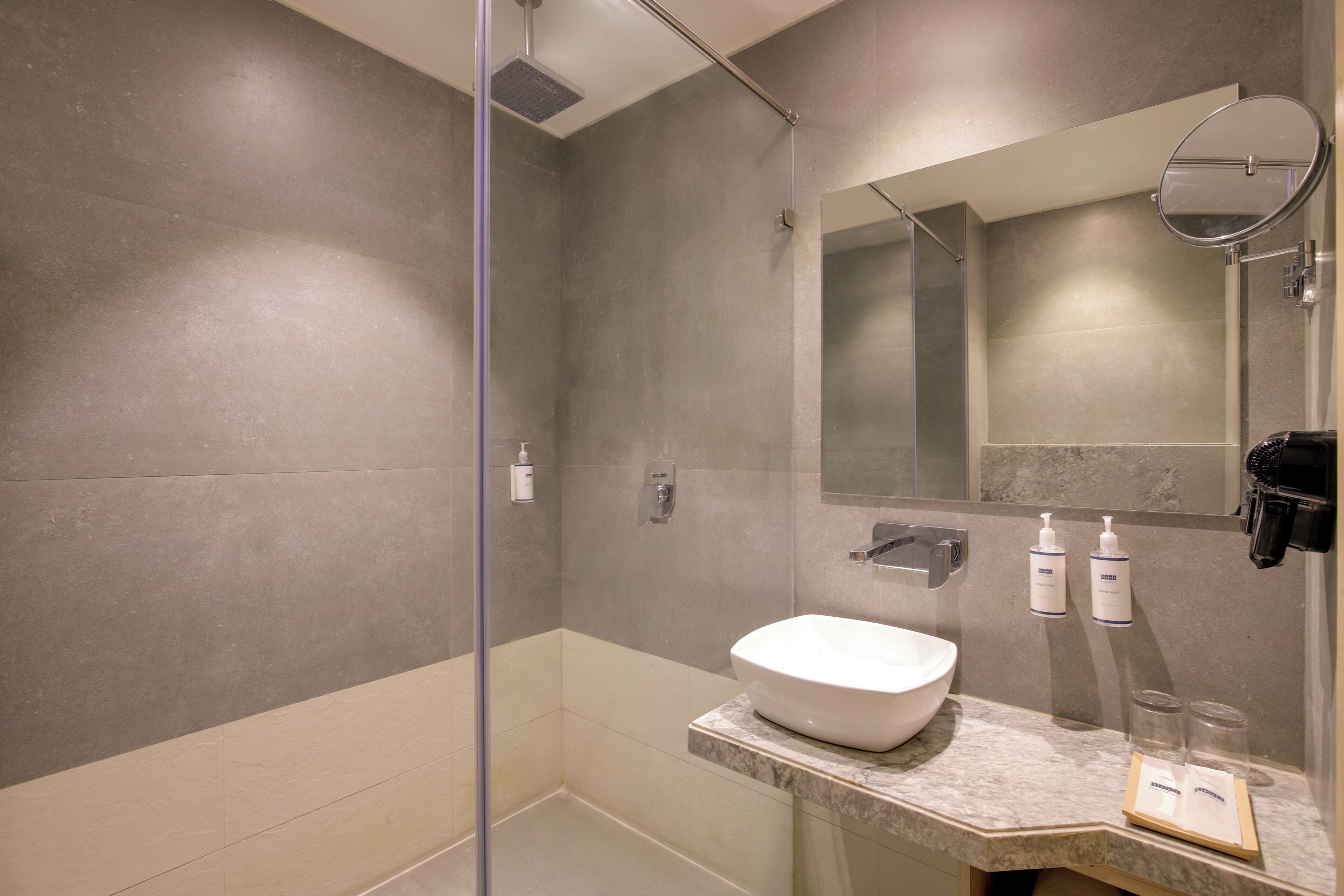 A modern bathroom with a glass-enclosed shower, a marble sink, and a large mirror.