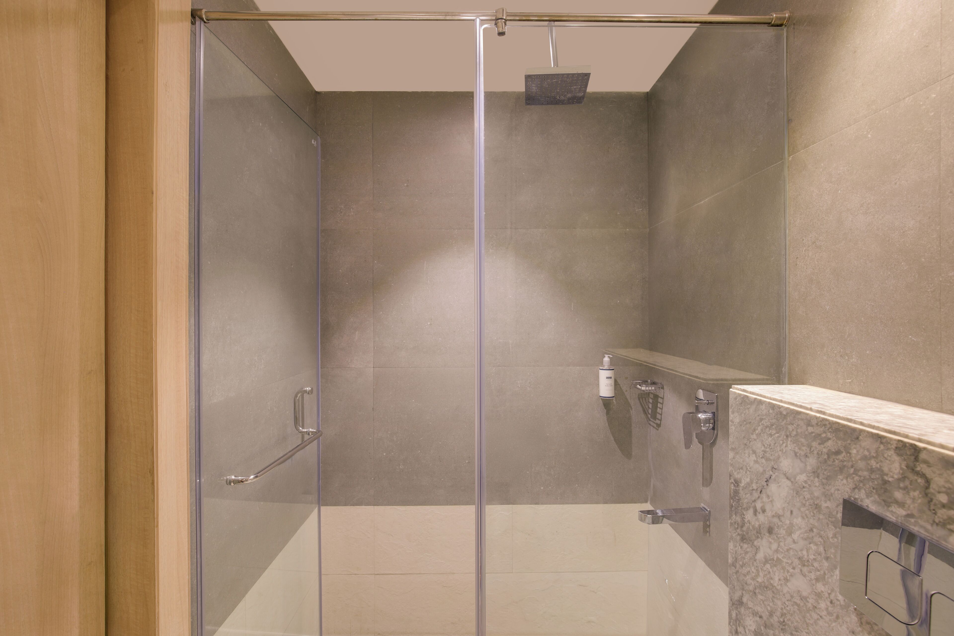 Cabina de ducha con paredes de vidrio, encimera de mármol y ducha de mano.