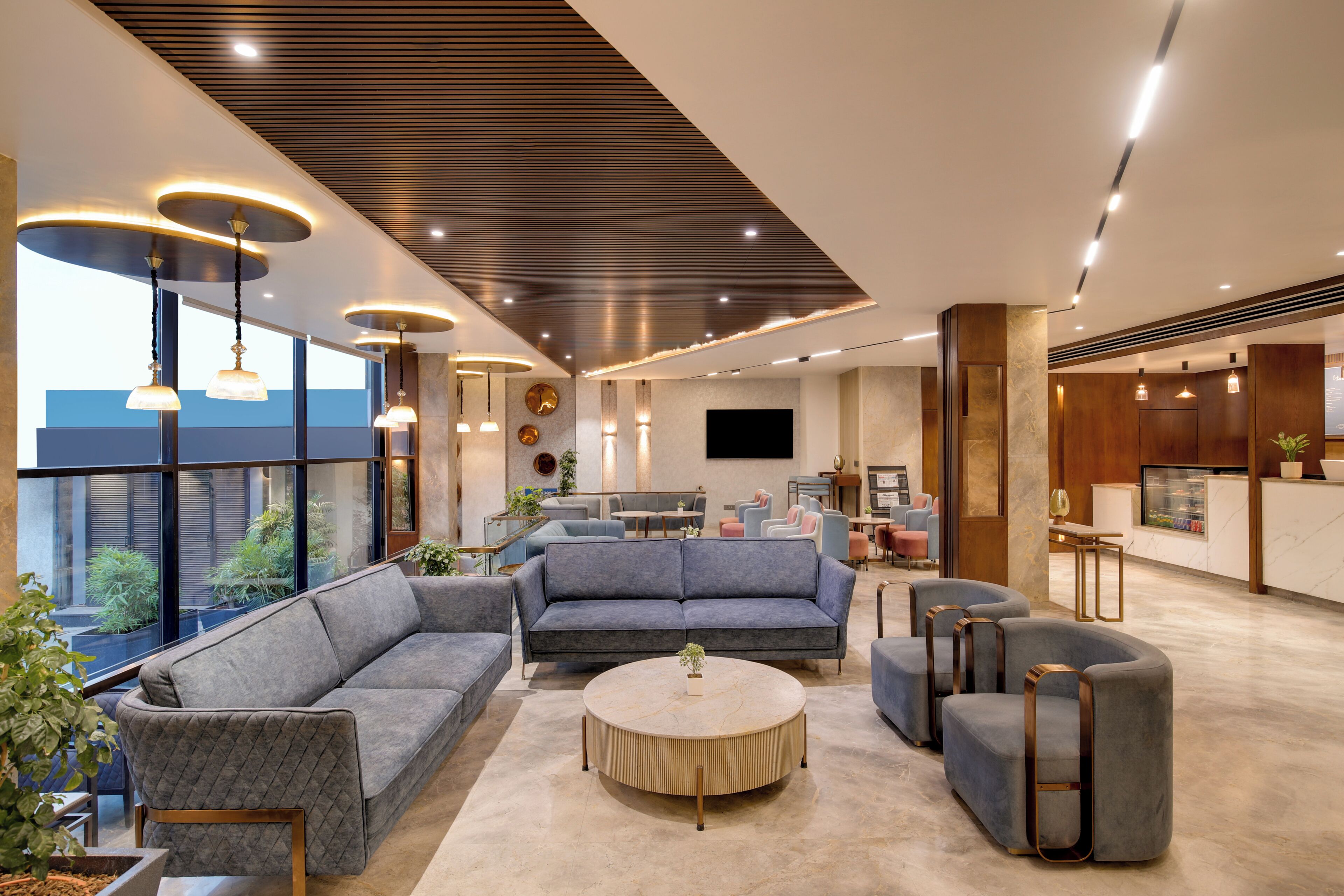 A modern hotel lobby with a seating area, a round table, and a kitchen in the background.