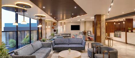 A modern hotel lobby with a seating area, a round table, and a kitchen in the background.