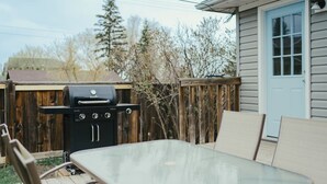 A backyard with a barbecue grill, a wooden deck, and a house with a blue door. - Beach Town Vibes • Relax & Unwind (Sylvan Lake)