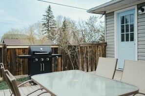 A backyard with a barbecue grill, a wooden deck, and a house with a blue door. - Beach Town Vibes • Relax & Unwind (Sylvan Lake)