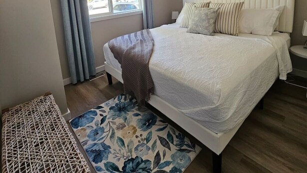 A bedroom with a bed, a window with curtains, a headboard, a bedside table, and a wall-mounted picture. - Beach Town Vibes • Relax & Unwind (Sylvan Lake)