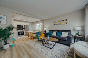 A modern living room with a sofa, coffee table, and a dining area with a table and chairs. - Beach Town Vibes • Relax & Unwind (Sylvan Lake)