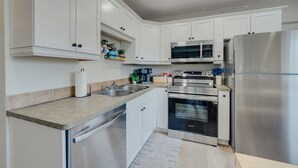 A modern kitchen with white cabinetry, stainless steel appliances, and a built-in oven. - Beach Town Vibes • Relax & Unwind (Sylvan Lake)