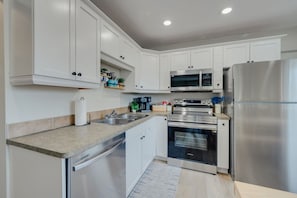 A modern kitchen with white cabinetry, stainless steel appliances, and a built-in oven. - Beach Town Vibes • Relax & Unwind (Sylvan Lake)