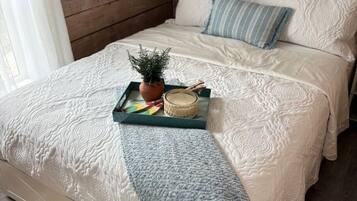 Un lit avec une couette blanche, un plaid bleu et un plateau sur lequel se trouvent une plante et une bougie.